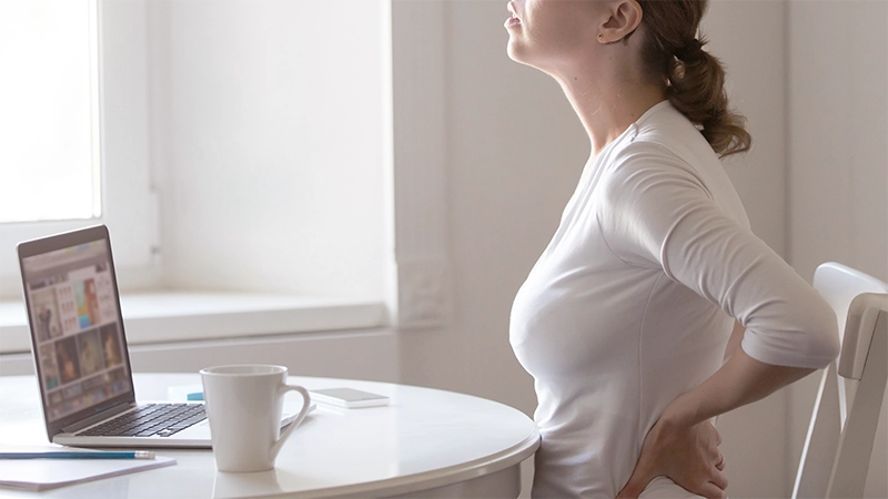 photo of an adult woman having lower back pain while working with a laptop