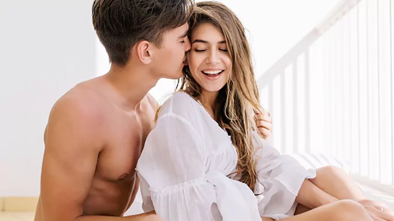 Photo of a girl blouse laughing while a boy with tanned skin kissing her cheek