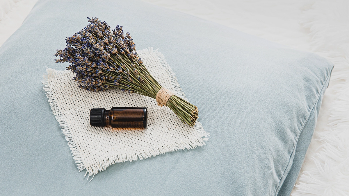 A small bottle of essential oil and a bundle of dried lavender flowers on a blue pillow, possibly used for natural bed bug prevention