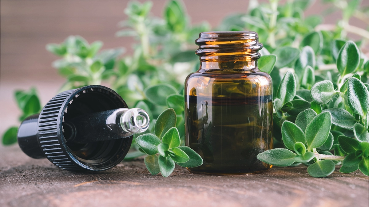 Bottle of thyme essential oil next to a thyme plant on a wooden table. Text on the bottle reads Organic Essential Thyme Oil